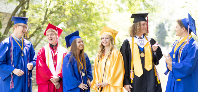 Students in varied colored graduation gowns talk and laugh together candidly.