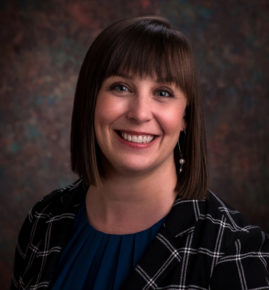 Andrea smiling at the camera wearing a plaid blazer and blue blouse.